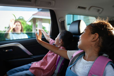 Cute girls waving at mother while sitting in car