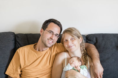 Portrait of smiling parents with baby boy relaxing on sofa at home