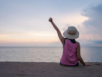Rear view of woman in hat at beach against sky