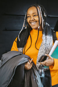 Smiling young woman holding jacket and books at community college