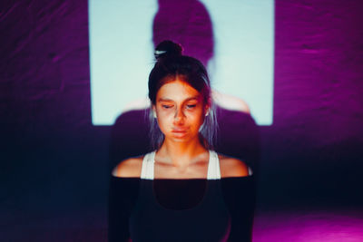 Portrait of young woman looking away while standing against wall