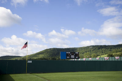 Baseball outfield fence and rolling hill with scoreboard and american flag