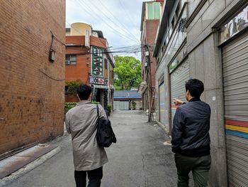 Rear view of man walking on footpath amidst buildings