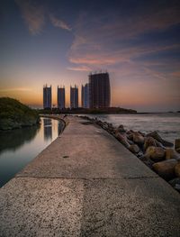 Sea by city buildings against sky during sunset