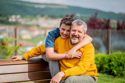 Portrait of father and son sitting on bench outdoors