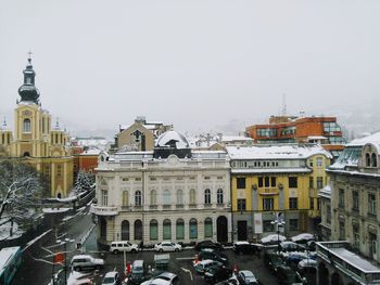 Cars on snow covered city against clear sky