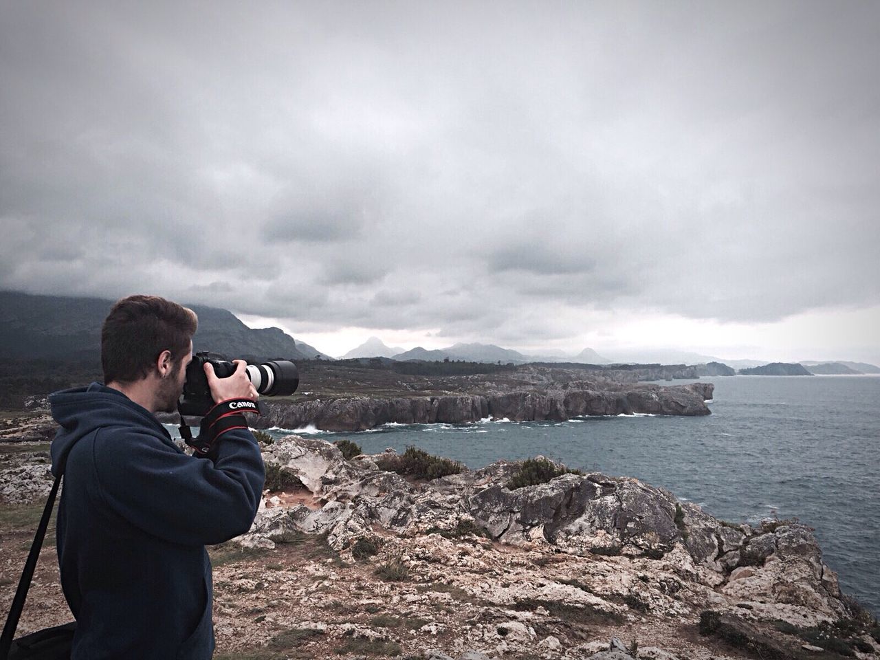 REAR VIEW OF MAN STANDING ON MOUNTAIN AGAINST CLOUDY SKY