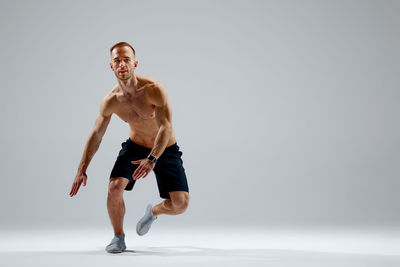 Full length of shirtless man jumping against white background