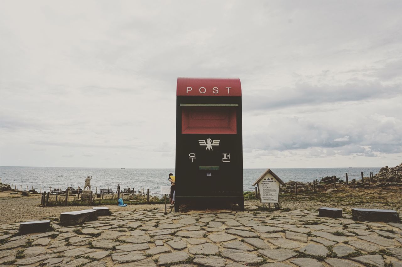 sea, communication, water, sky, tranquil scene, horizon over water, tranquility, scenics, cloud, calm, idyllic, information sign, ocean, cloud - sky, nature, outdoors, beauty in nature, message, tall - high, in front of, cloudy, shore, remote