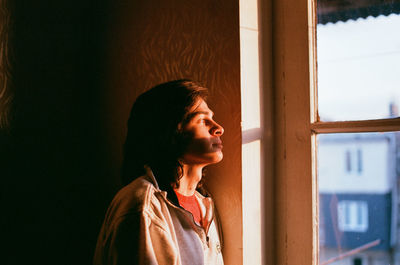 Young woman looking through window at home