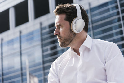 Businessman sitting in front of office building, wearing headphones