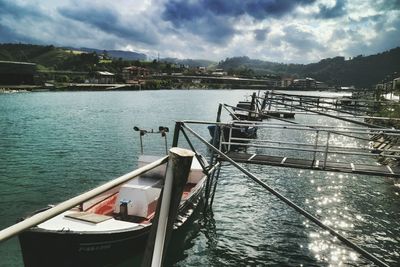 Boats in river against cloudy sky