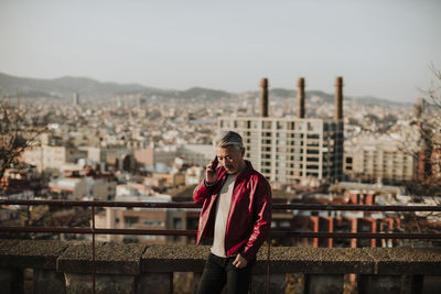 Man standing by railing against buildings in city