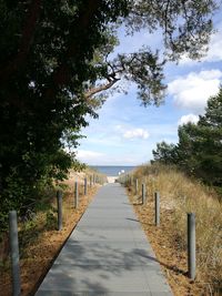 Empty footpath by road against sky