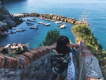 Rear view of woman standing on rock by sea