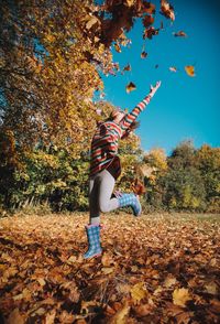 Cheerful girl throwing autumn leaves at park