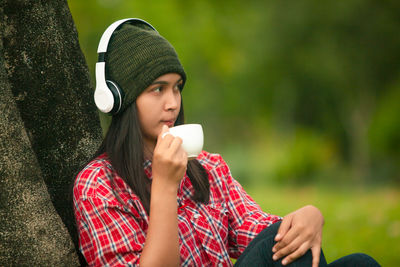 Young woman wearing headphones and drinking coffee