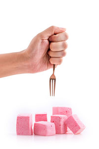 Close-up of hand grabbing marshmallows with fork on over white background