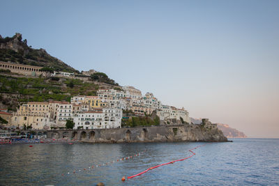 Buildings by sea against clear sky