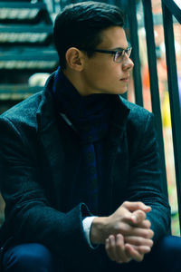 Young man looking away while sitting outdoors