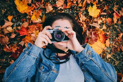 Midsection of woman photographing with autumn leaves