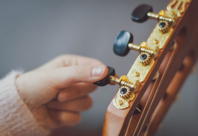 The girl twists the guitar peg while tuning the strings.