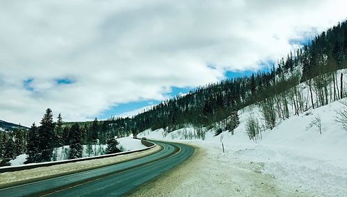 Snow covered road amidst trees against sky