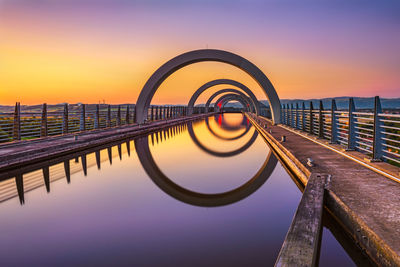 Reflection of pier on sea against sky during sunset