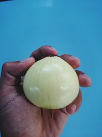 Close-up of hand holding apple against blue background