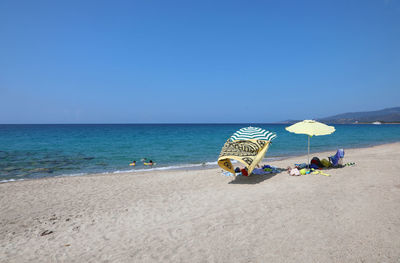 Deck chairs on beach against clear blue sky