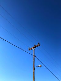 Low angle view of electricity pylon against clear blue sky