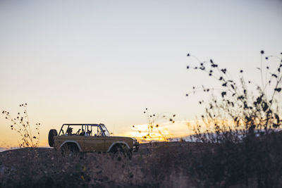 Woman sitting in off-road vehicle against sky during sunset