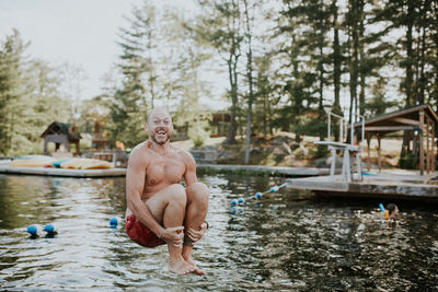 Full length portrait of shirtless man jumping in lake