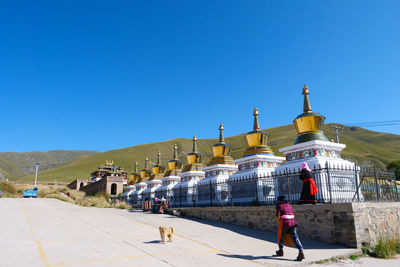 People in front of building against clear blue sky