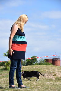 Pregnant woman with dog standing against sky