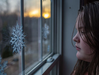Close-up of girl looking through window at home