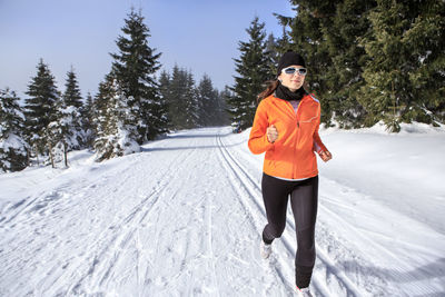 Woman running on snow covered field against sky