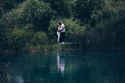 Woman standing by lake against trees