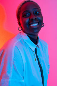 Delighted african american female smiling in studio with colorful neon lights and looking away