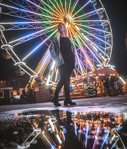 Man standing by illuminated ferris wheel against sky at night