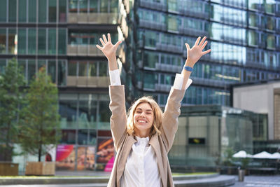 Portrait of woman with arms raised in city