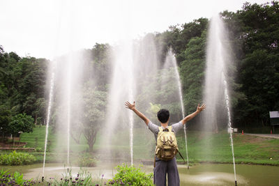 Rear view of woman with arms outstretched standing against fountain at park