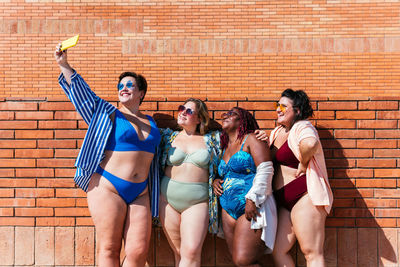 Full length of smiling friends standing against brick wall