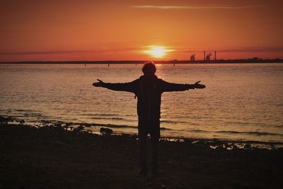 Silhouette of man with arms raised on beach at sunset