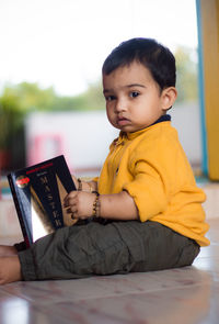 Portrait of cute girl playing with book while sitting on floor at home