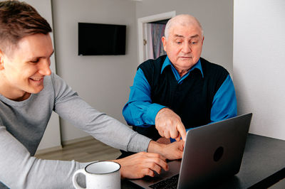 Smiling grandson sharing laptop with grandfather at home