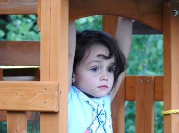 Cute girl looking away while hanging on wood in playground