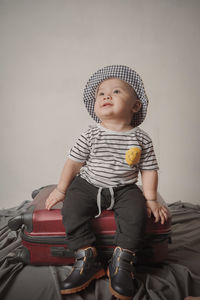 Cute baby sitting on red suitcase on white background, travel concept.