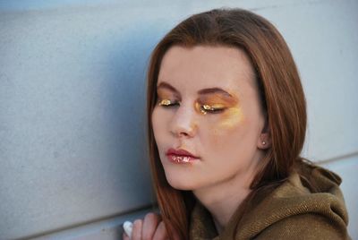 Close-up of young woman with make-up against wall