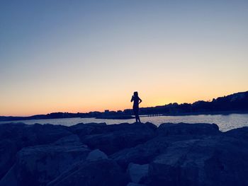 Silhouette woman standing on rock at beach against clear sky